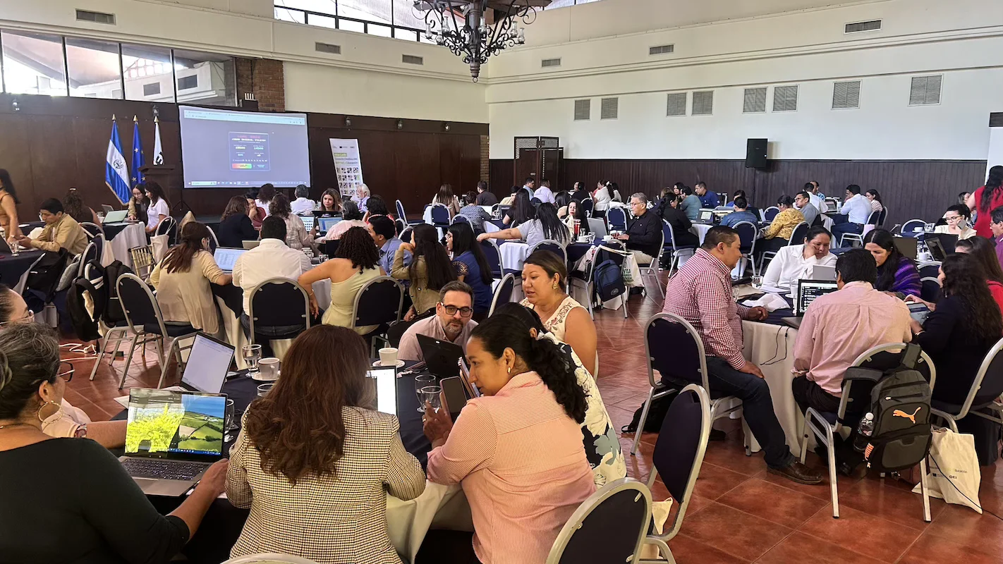 Salón lleno de asesores trabajando en equipo con sus computadores durante la jornada de cierre del programa en San Salvador